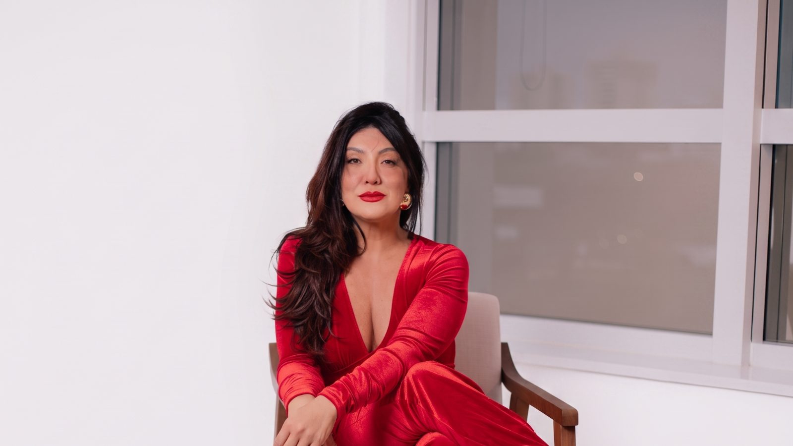 Luiziana Malheiros sentada, de vermelho, olhando para a câmera